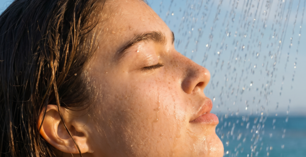 Mujer bajo una ducha exterior en la playa con la piel mojada, imagen para explicar cómo el agua con cal, el cloro o la sal pueden influir en la sensación de piel tirante
